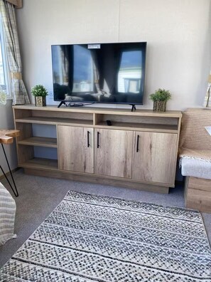 Ein Wohnzimmer mit einem Flachbildfernseher an einem Holzschrank, einem gemusterten Teppich und einer Couch.