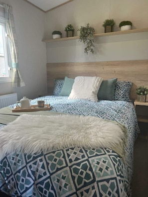 Ein Schlafzimmer mit einem gemusterten Bettbezug, einer flauschigen weißen Decke und einem Nachttisch mit Tasse und Untertasse.