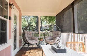 Un porche cubierto con dos sillones acolchados, una mesa y una planta en maceta.