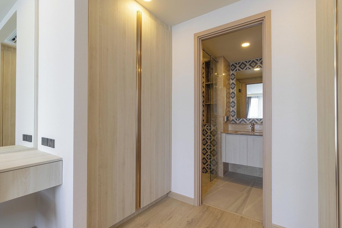 Un couloir avec une armoire en bois, un miroir et une porte donnant sur une salle de bain dont le sol est recouvert de carreaux décoratifs.