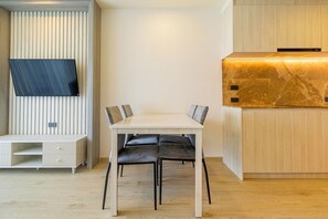 Moderni keittiö, jossa on sisäänrakennettu liesi, ruokapöytä tuoleineen sekä seinälle asennettu taulutelevisio.