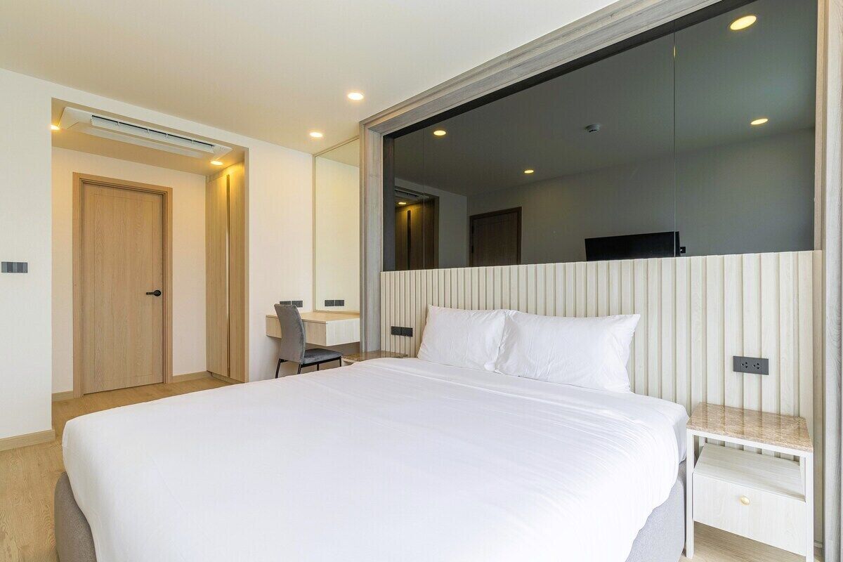 A modern hotel room with a large bed, a desk, and a mirror.