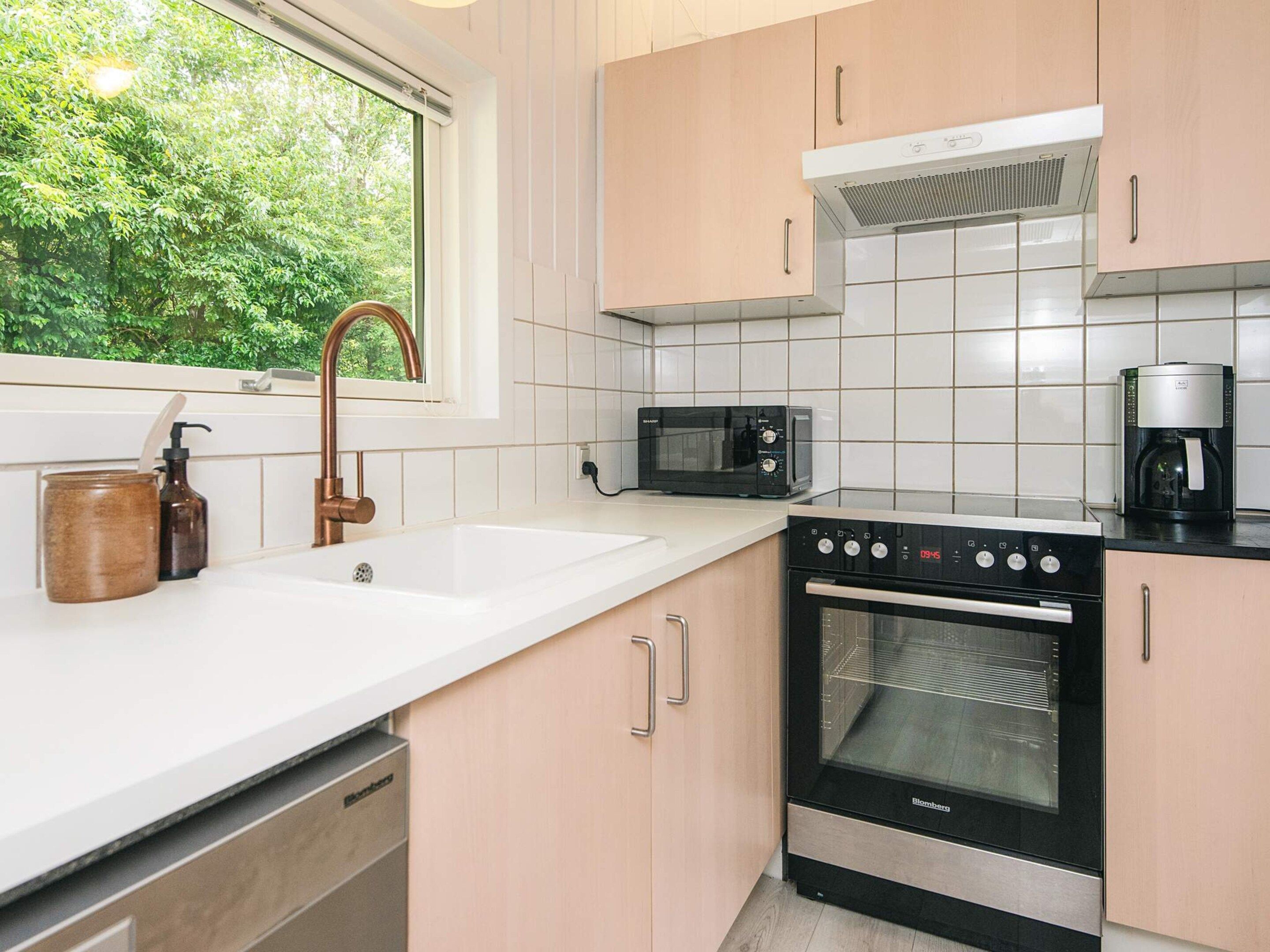 A kitchen with a sink, faucet, microwave, coffee maker, oven, and cabinets.