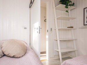 Quarto com cama, porta branca, estante escada branca e uma planta.