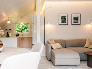 A modern living room with a sofa, a dining table, and a kitchen area with cabinets and a window. - 4 Star Holiday Home in Silkeborg (Silkeborg)