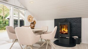 Un intérieur moderne avec une table ronde, quatre chaises, une cheminée et une vue sur l’extérieur.