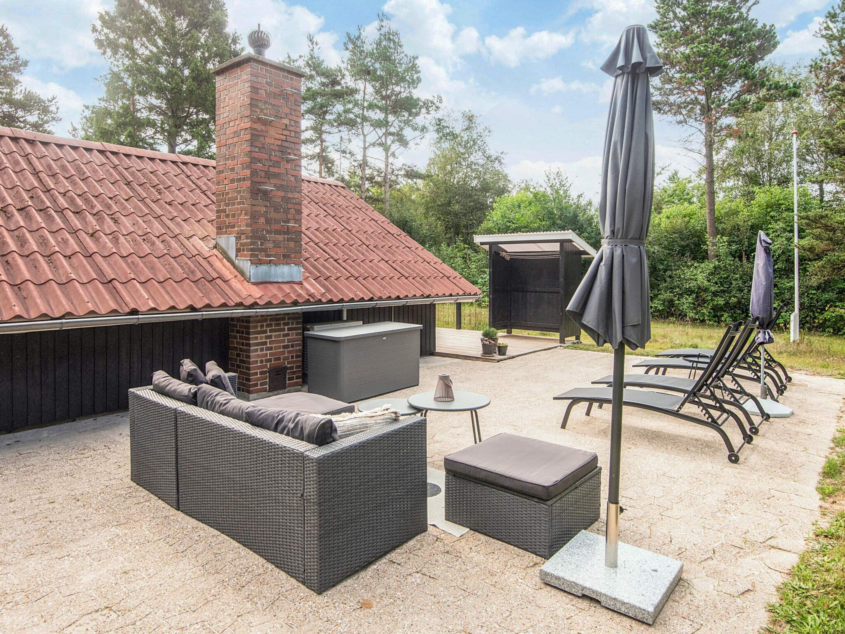 An outdoor patio area with a brick fireplace, a sofa, a table, and a grill.