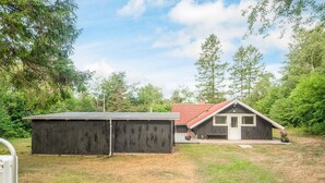 Une maison de plain-pied avec un toit rouge, un abri en bois et une cour couverte d’herbe.