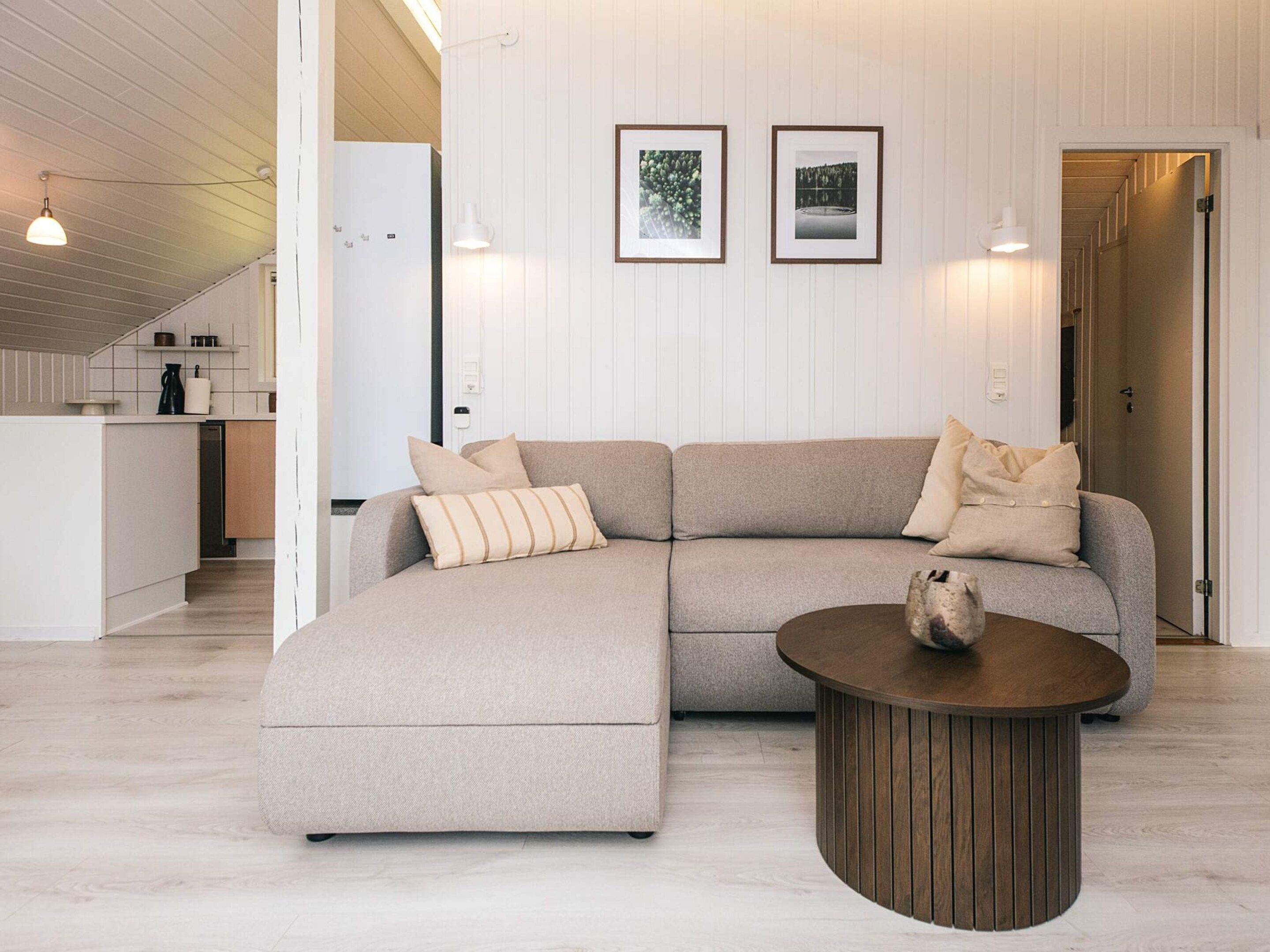 Una sala moderna con un sofá modular, una mesa de centro redonda y una cocina al fondo.