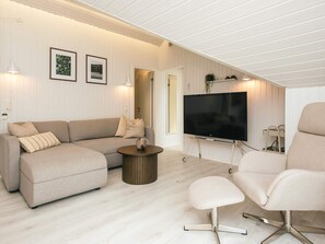 Ein modernes Wohnzimmer mit einer Couch, einem Couchtisch, einem Fernseher auf einem Schrank und einem Sessel.