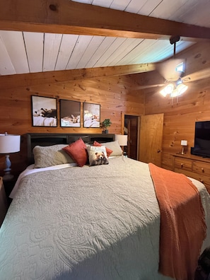 Ein Schlafzimmer mit Holzwänden, einem großen Bett, zwei Wandleuchten und gerahmten Bildern.