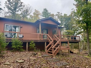 Eine Holzhütte mit einer Holzterrasse, einer Treppe und einem großen Fenster.