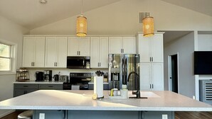 Una cocina moderna con armarios blancos, una isla grande con taburetes, electrodomésticos de acero inoxidable y dos lámparas colgantes.