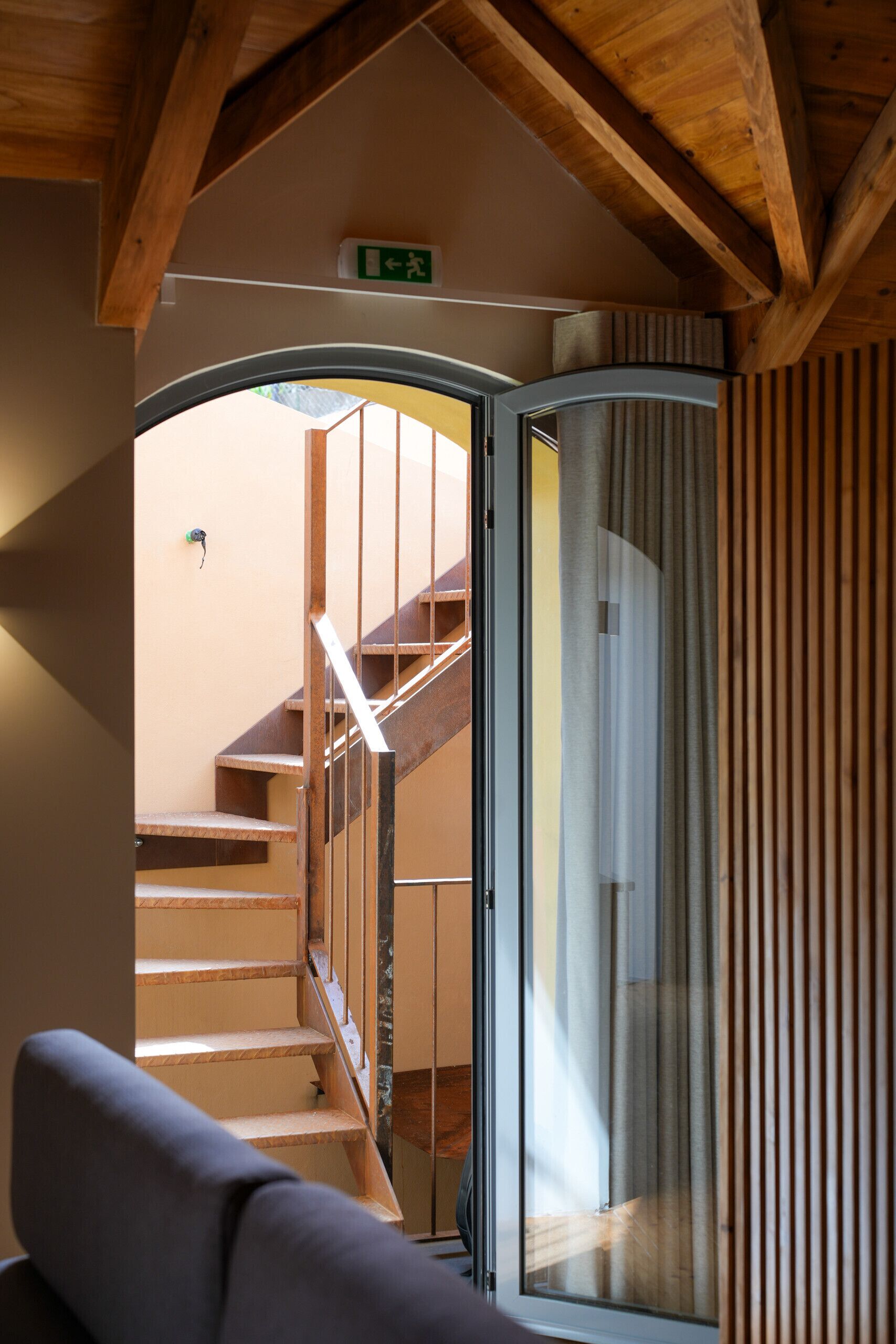 Un escalier en bois menant à l’étage supérieur, une porte-fenêtre coulissante et un canapé dans un intérieur moderne.