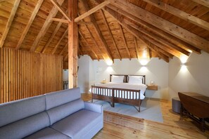 Une chambre avec un plafond en bois, un lit, une table de chevet, une lampe fixée au mur et un canapé gris.