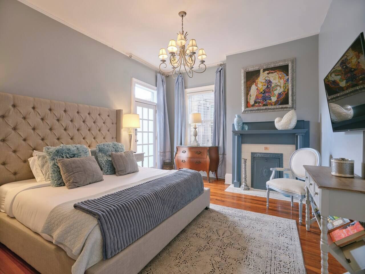 Um quarto com uma cama grande, um lustre, uma lareira e um quadro na parede.