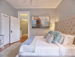 Ein Schlafzimmer mit einem großen Bett, einem Gemälde eines Bootes auf dem Wasser, einer Kandelaber und einer Tür zu einem anderen Raum.