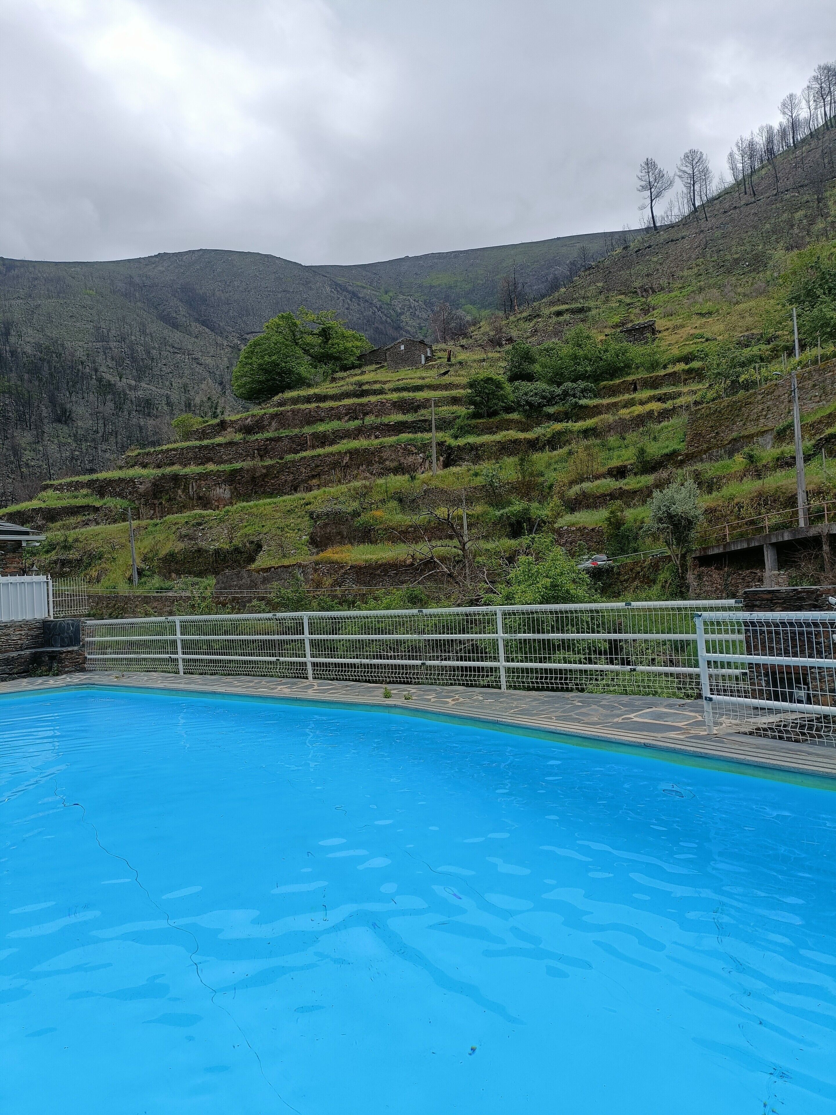 Una piscina con una recinzione bianca e un paesaggio collinare sullo sfondo.