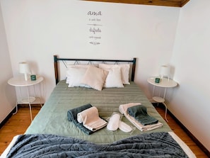 Een keurig opgemaakt slaapkamer met een bed, kussens, een nachtkastje, een wandklok en een bedlampje.