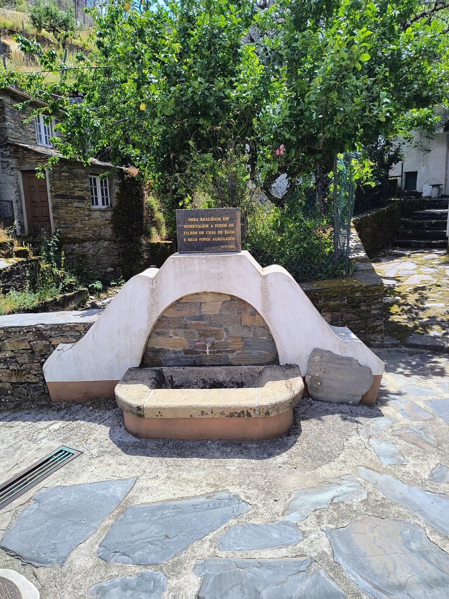 A stone structure with a plaque, surrounded by greenery and stone steps.