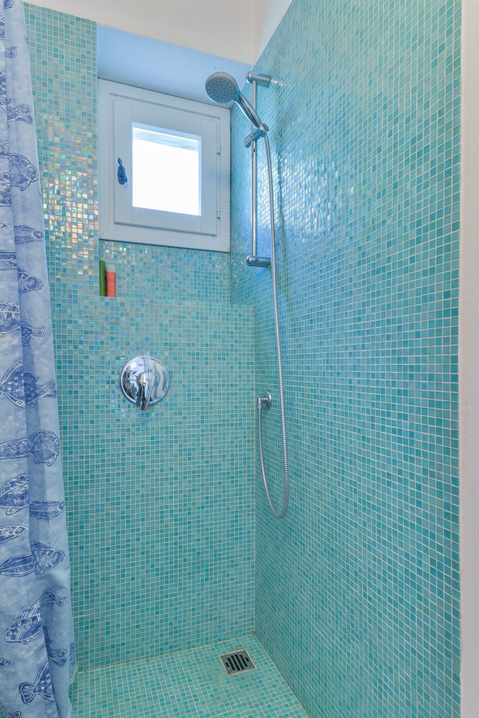 Eine Dusche mit Duschbrause, Wandarmatur und kleinem Fenster darüber.