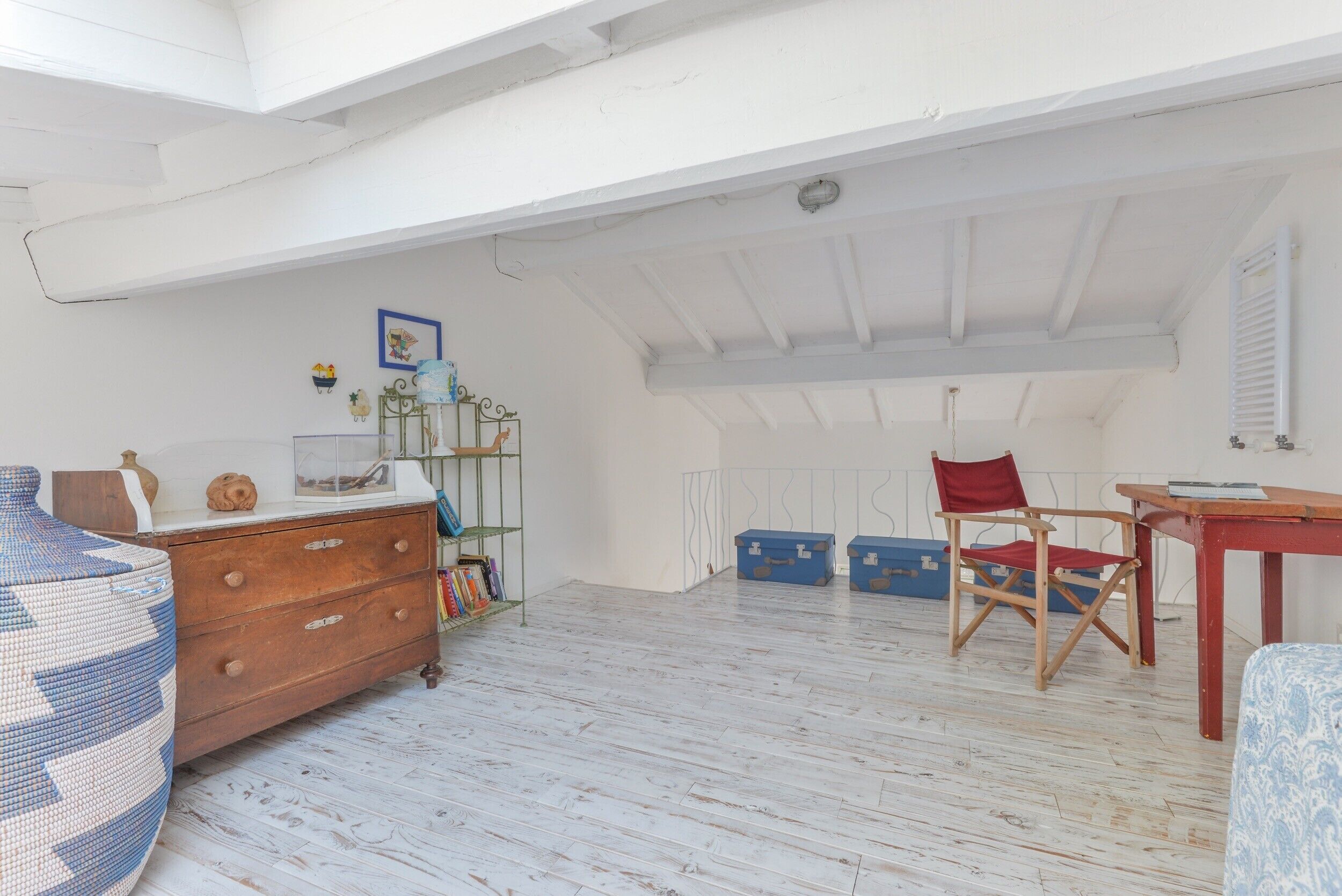 A room with a wooden dresser, a chair, a table, and a shelf with books and decorative items.