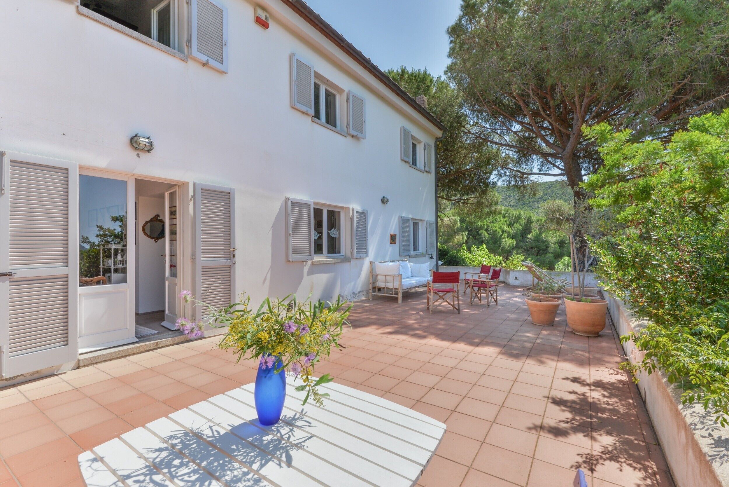 Une maison à deux étages avec un patio, un vase bleu rempli de fleurs et un coin repas aménagé avec du mobilier d’extérieur.