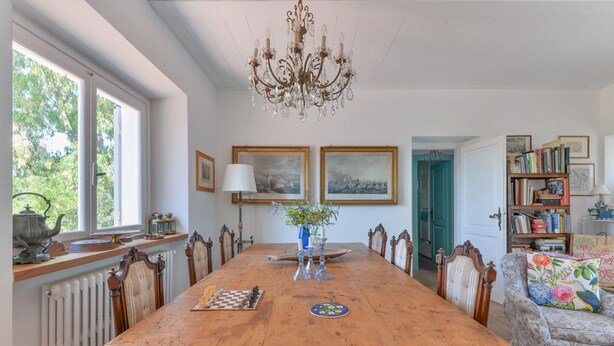 Ein Esszimmer mit Holztisch, Stühlen, einer Chandelierleuchtre und gerahmten Kunstwerken an den Wänden.