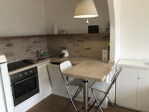 A compact kitchen with a stove, oven, sink, and a dining area with a table and chairs. - Holiday Home 'Terrazza sul Mare' with Sea View and Private Terrace (Marina di Campo)
