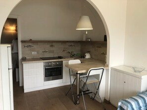 Een compacte keuken met een inbouwoven, een spoelbak en een klein eethoekje met een stoel.