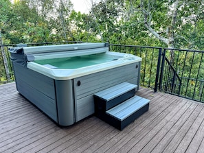 A hot tub on a wooden deck with a metal railing, surrounded by trees. - The Idlewylde Retreat: Woodland Charm, Mountain Views, & Hot Tub (Morrilton)