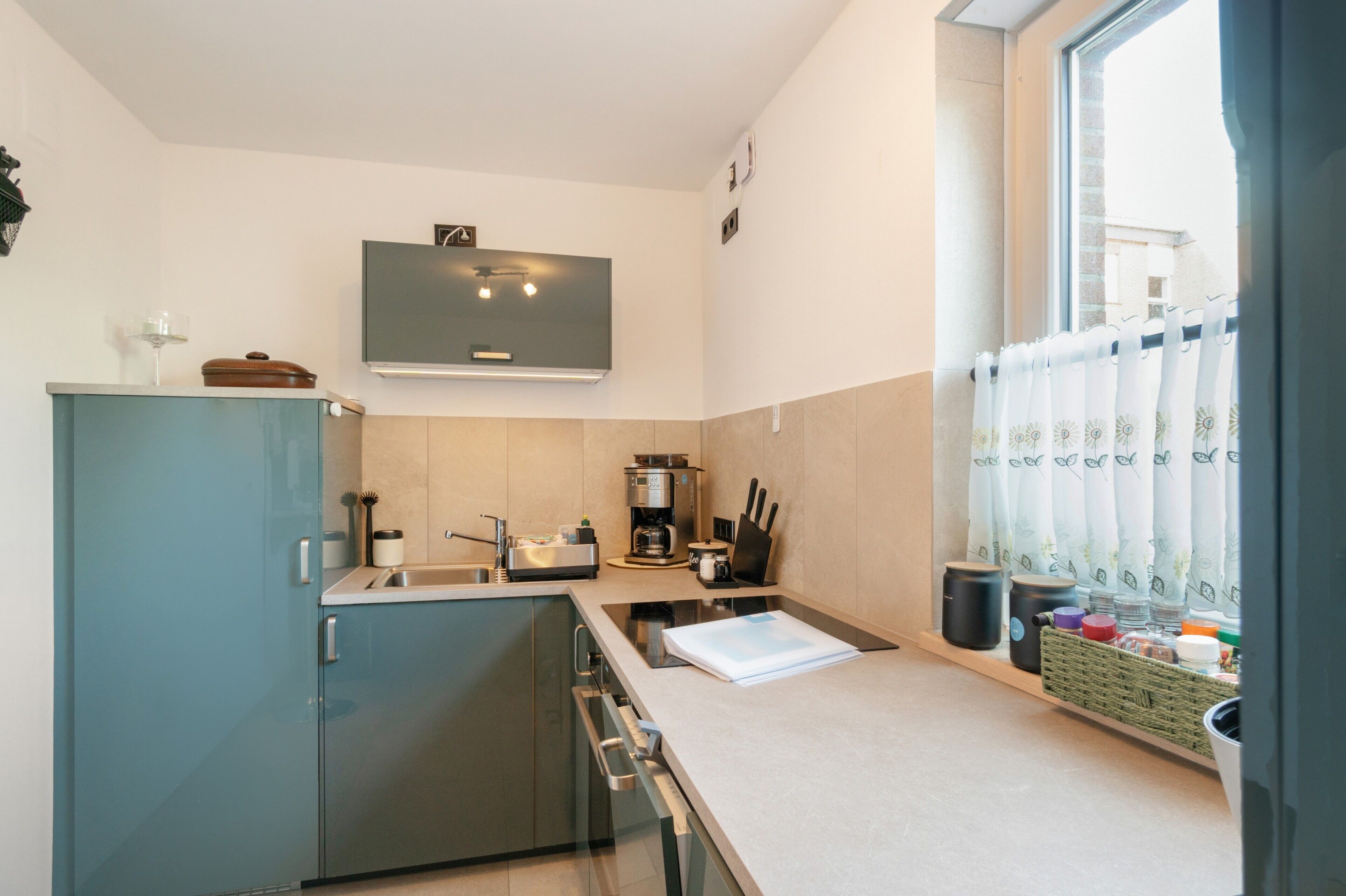 Eine moderne Küche mit Backofen, Kaffeemaschine und einem Fenster mit Vorhängen.