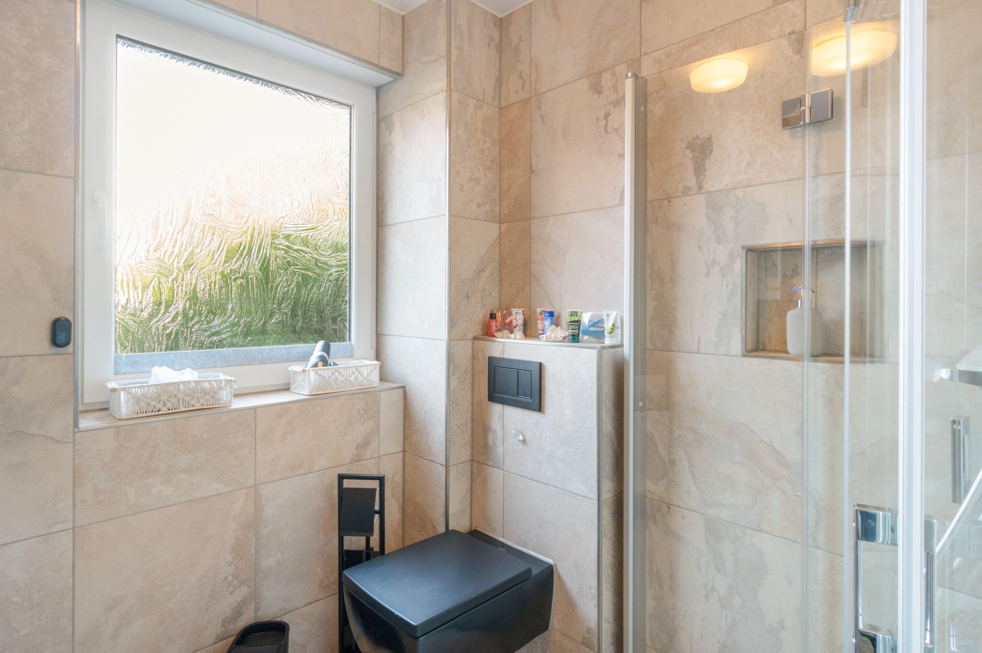 Ein modernes Badezimmer mit Duschkabine aus Glas, einem Fenster mit Blick auf Grünflächen und einer kleinen Sitzbank.