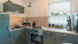 Een compacte keuken met een inbouwoven, een koffieapparaat en een raam met uitzicht op groen.