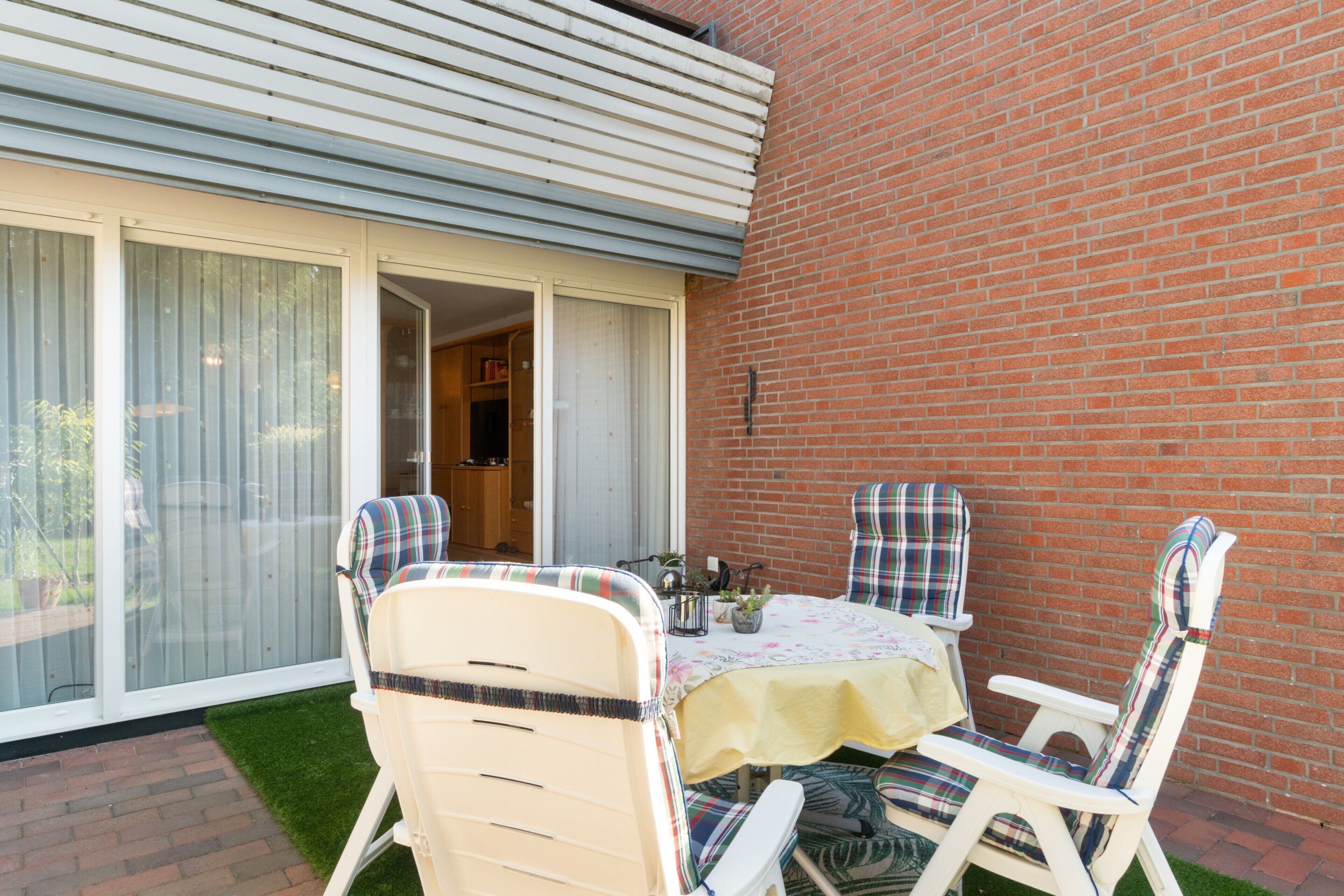 Eine Terrasse mit Tisch und Stühlen, eine Ziegelmauer und eine Glastür, die sich öffnen lässt.