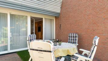 Eine Terrasse mit Tisch und Stühlen, eine Ziegelmauer und eine Glastür, die sich öffnen lässt.