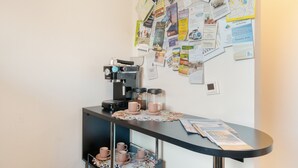 Een koffiehoek met een koffieapparaat, kopjes en een muur vol verschillende papieren en mededelingen.