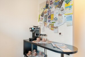 Ein Kaffee-Bereich mit Kaffeemaschine, Tassen und einer Wand voller verschiedener Papiere und Aushänge.