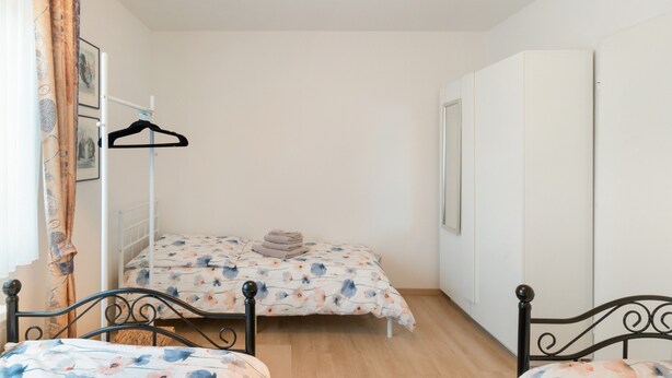 Een kleine, net kamer met een enkel bed, een garderobe en een kledingrek.