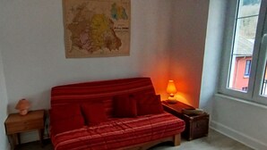 A room with a red sofa, a small wooden side table with a lamp, and a map on the wall. - Mountain Charm in La Bourboule - Apartment with Terrace and Small Garden (La Bourboule)
