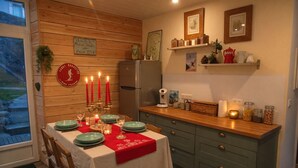 A cozy kitchen with a dining table set for four, a refrigerator, and various kitchen items on the counter. - Mountain Charm in La Bourboule - Apartment with Terrace and Small Garden (La Bourboule)