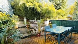 A wooden deck with a table and chairs, surrounded by potted plants and a stone wall. - Mountain Charm in La Bourboule - Apartment with Terrace and Small Garden (La Bourboule)