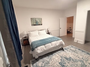 A bedroom with a bed, bedside lamps, a rug, and a door leading to another room.