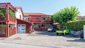 Ein Gebäude mit roter Fassade, einem überdachten Eingang und einem Parkplatz mit einem grünen Auto und Fahrrädern.