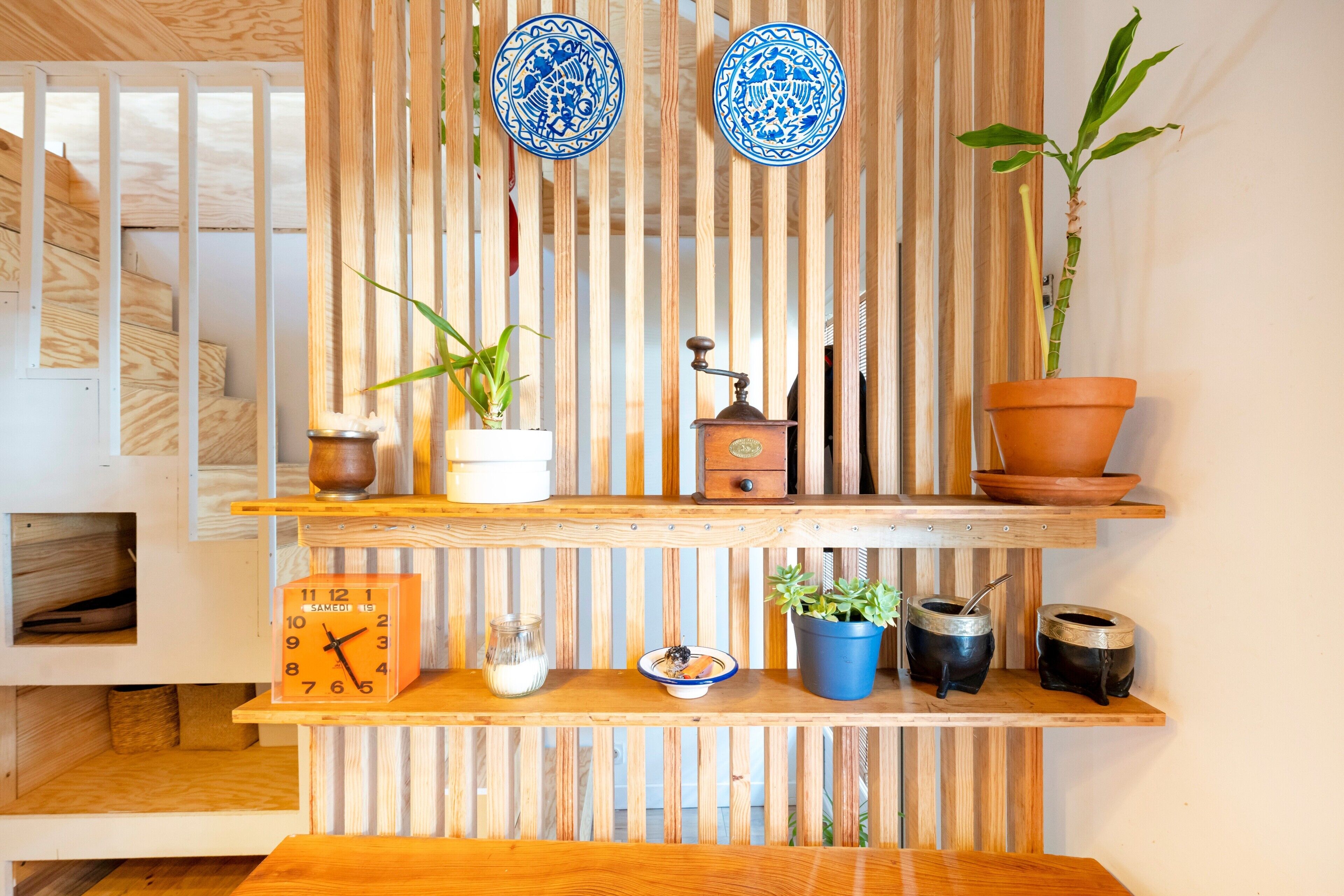 Una repisa de madera con un reloj, un pequeño florero, un cuenco y plantas en macetas.