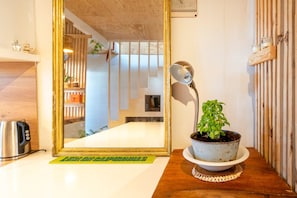 Ein Zimmer mit Holzboden, einer Topfpflanze, einem Wasserkocher, einem gerahmten Spiegel und einem kleinen Regal mit Dekoration.
