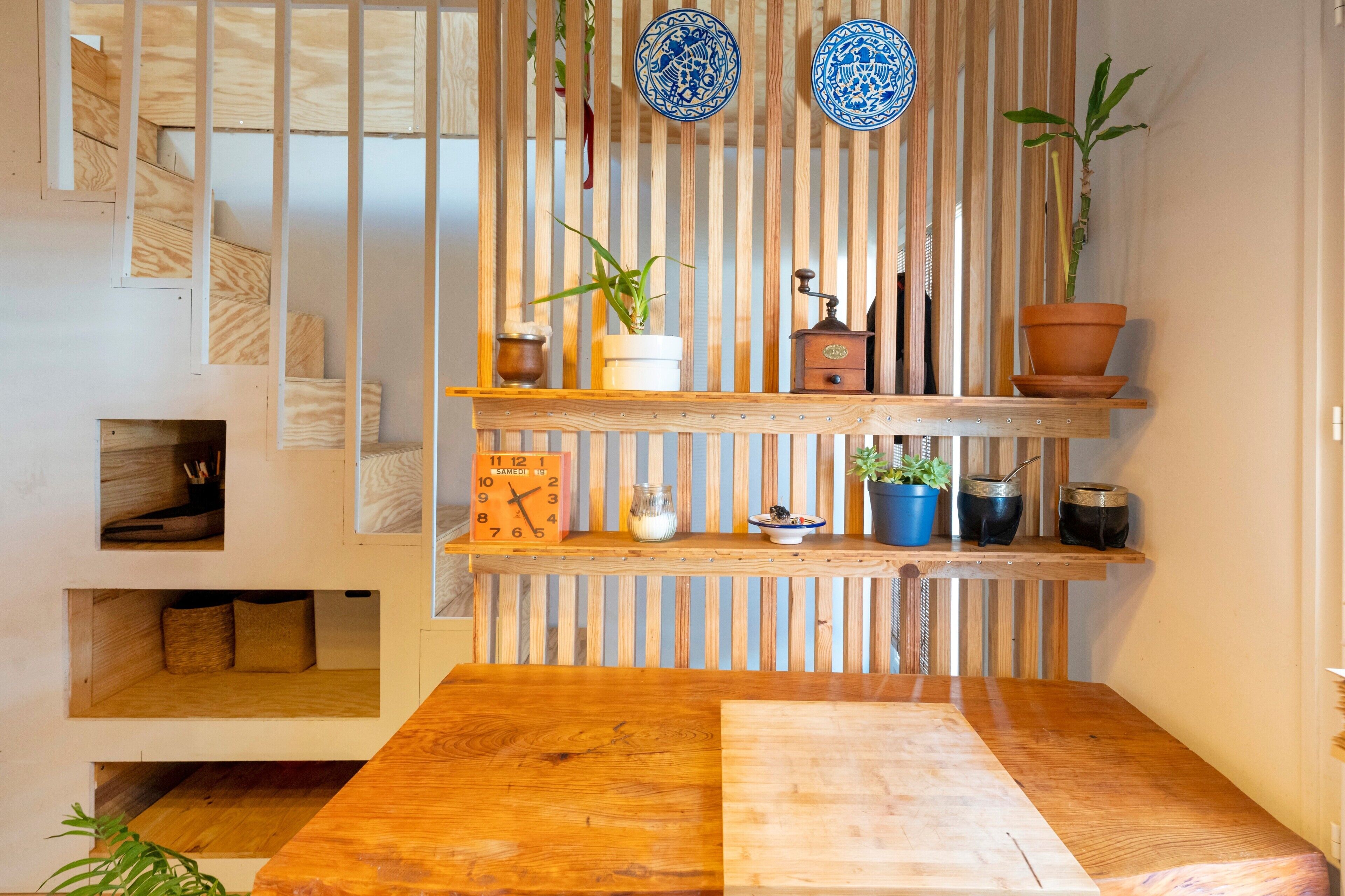 Un intérieur moderne avec une table en bois, des étagères ornées d’objets décoratifs et une horloge.