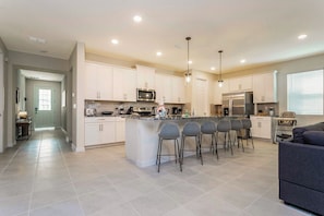 A spacious kitchen with white cabinets, a central island with bar stools, a refrigerator, and a microwave. - Modern 9BR Family Villa Pool and Relax (Kissimmee)