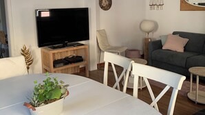 Ein Wohnzimmer mit Flachbildfernseher, einem runden Esstisch, einer Couch und einem kleinen Beistelltisch.