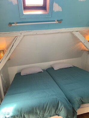 Ein kleines Zimmer mit einem Einzelbett, einem Dachfenster, weißen Wänden und einem schlichten, klaren Design.